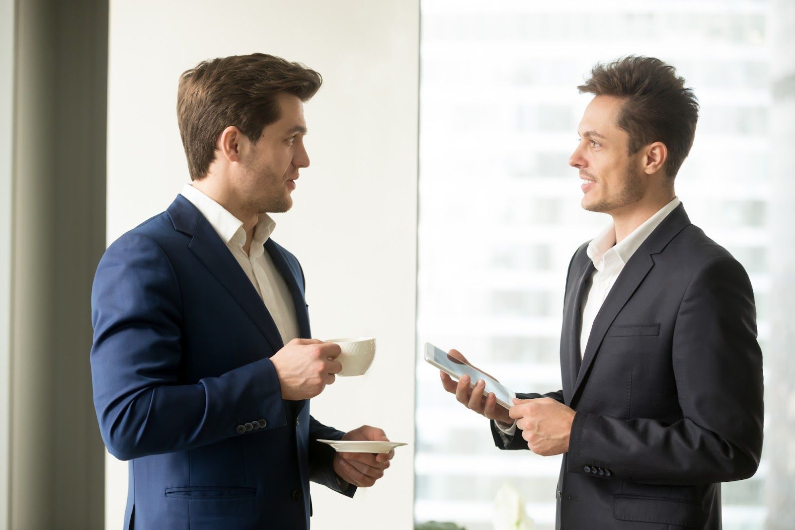 Two men in suits holding cups and a phoneAI-generated content may be incorrect.